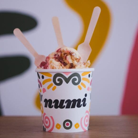 A paper cup of Numi ice cream with wooden spoons