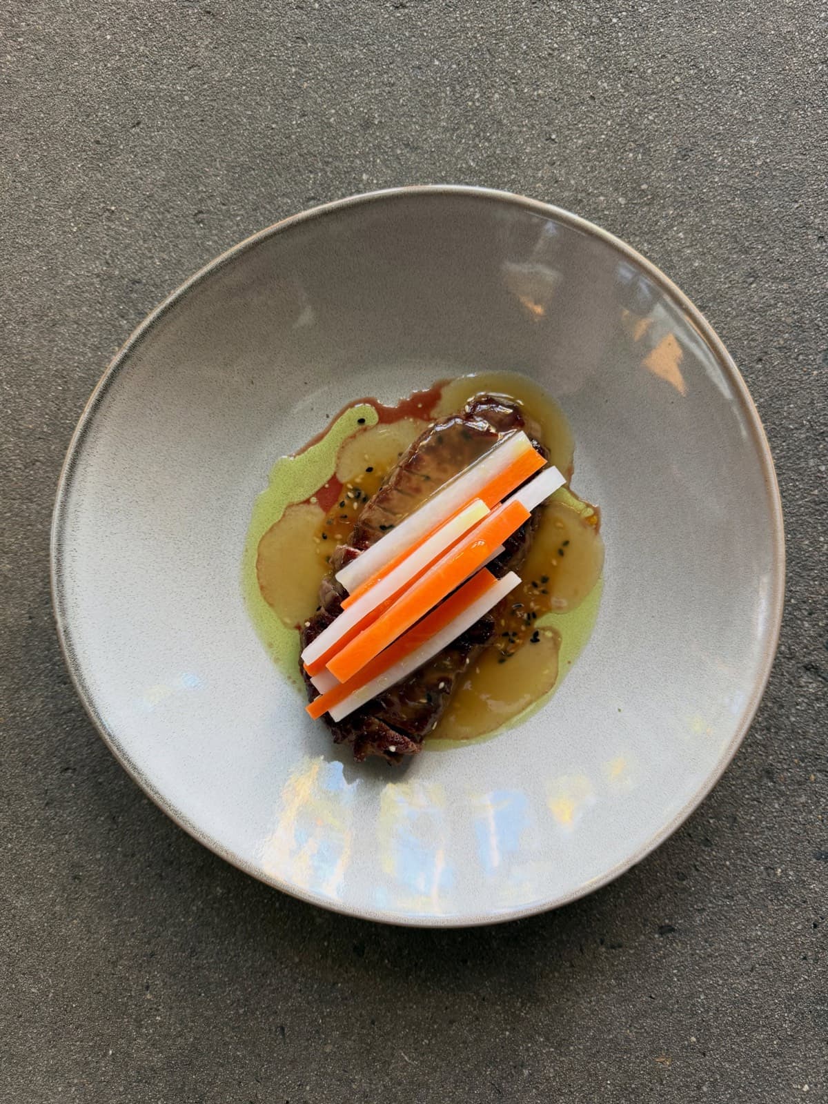 BBQ striploin in dashi with miso caramel and a stack of pickled daikon and carrot, in a pale ceramic bowl
