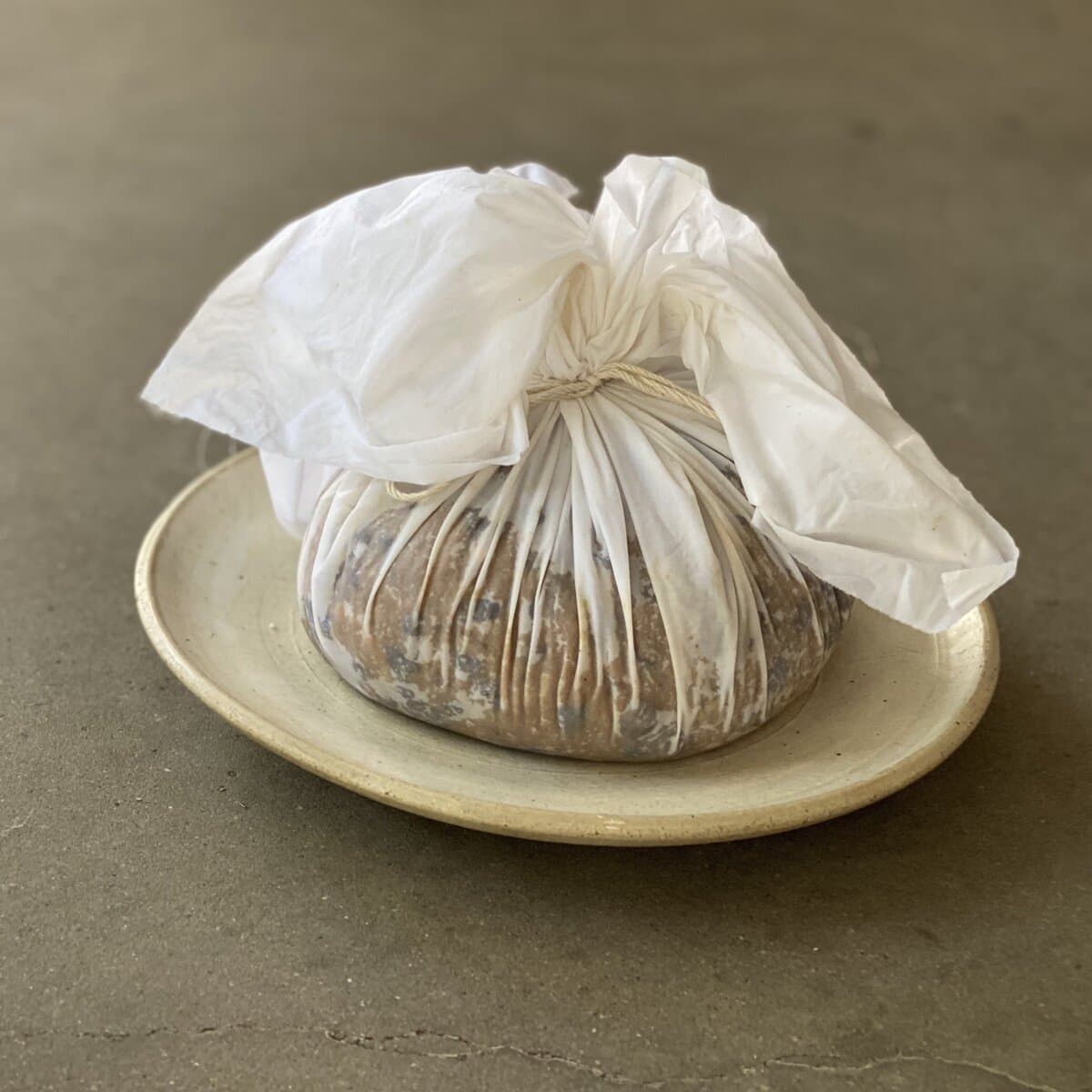 A Nu Nu Christmas pudding tied up in white paper with string, on a stoneware plate